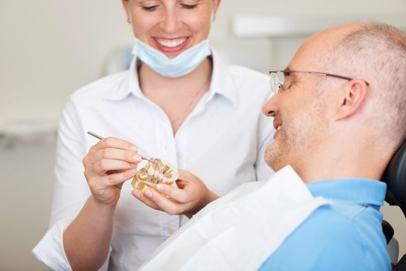 21246833 - smiling female dentist explaining artificial teeth to patient in clinic